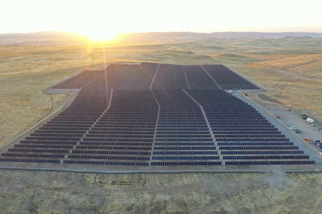 California large-scale solar PV farm, or power plant, with a bright sun setting on the horizon behind it. 