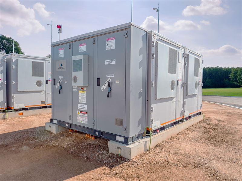 A grey-coloured containerised battery storage system unit from Wartsila's GridSolv Quantum range sits on concrete in an outdoor project setting. 