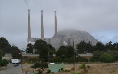 Smokestacks at Morro Bay, California, pictured before the plant shut down in 2014. Behind it is the volcanic plug Morro Rock, which has protected status and faces the beach in front of the stacks. Image: Wikimedia user Robert Ashworth.